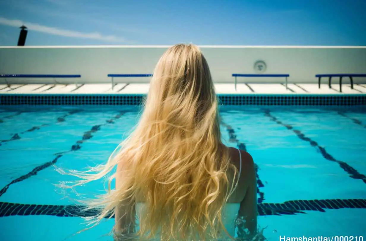 Olivenöl auf Kopfhaut über Nacht, Blondes Modell, Rückansicht, sie steht in einem Pool, trägt weißen Badeanzug, hellblaues Wasser